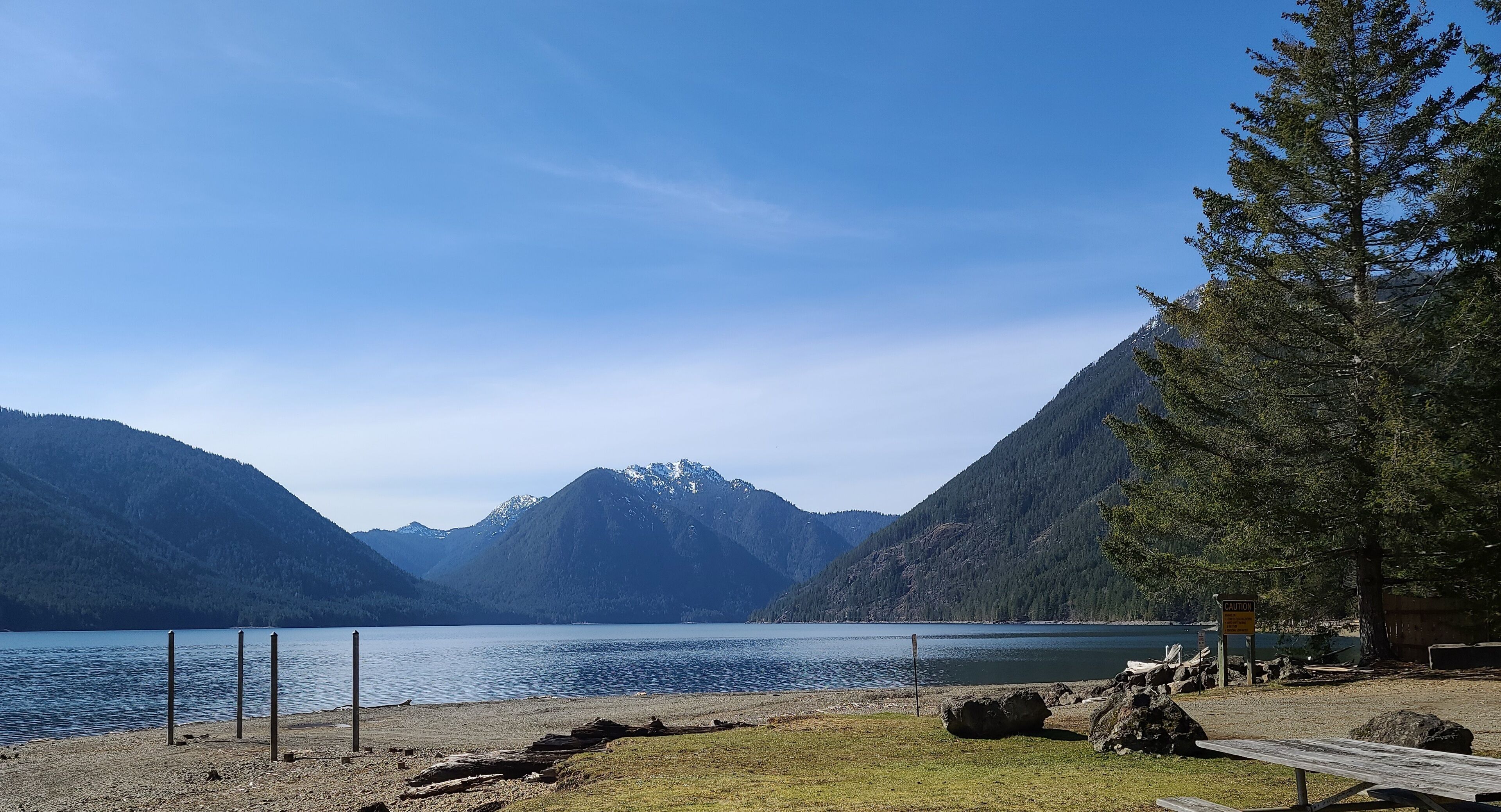Une vue sur le lac, avec des montagnes en arrière-plan, une table de pique-nique et un panneau d’avertissement.