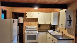 A compact kitchen with wooden cabinets, a white refrigerator, a stove, and a sink.