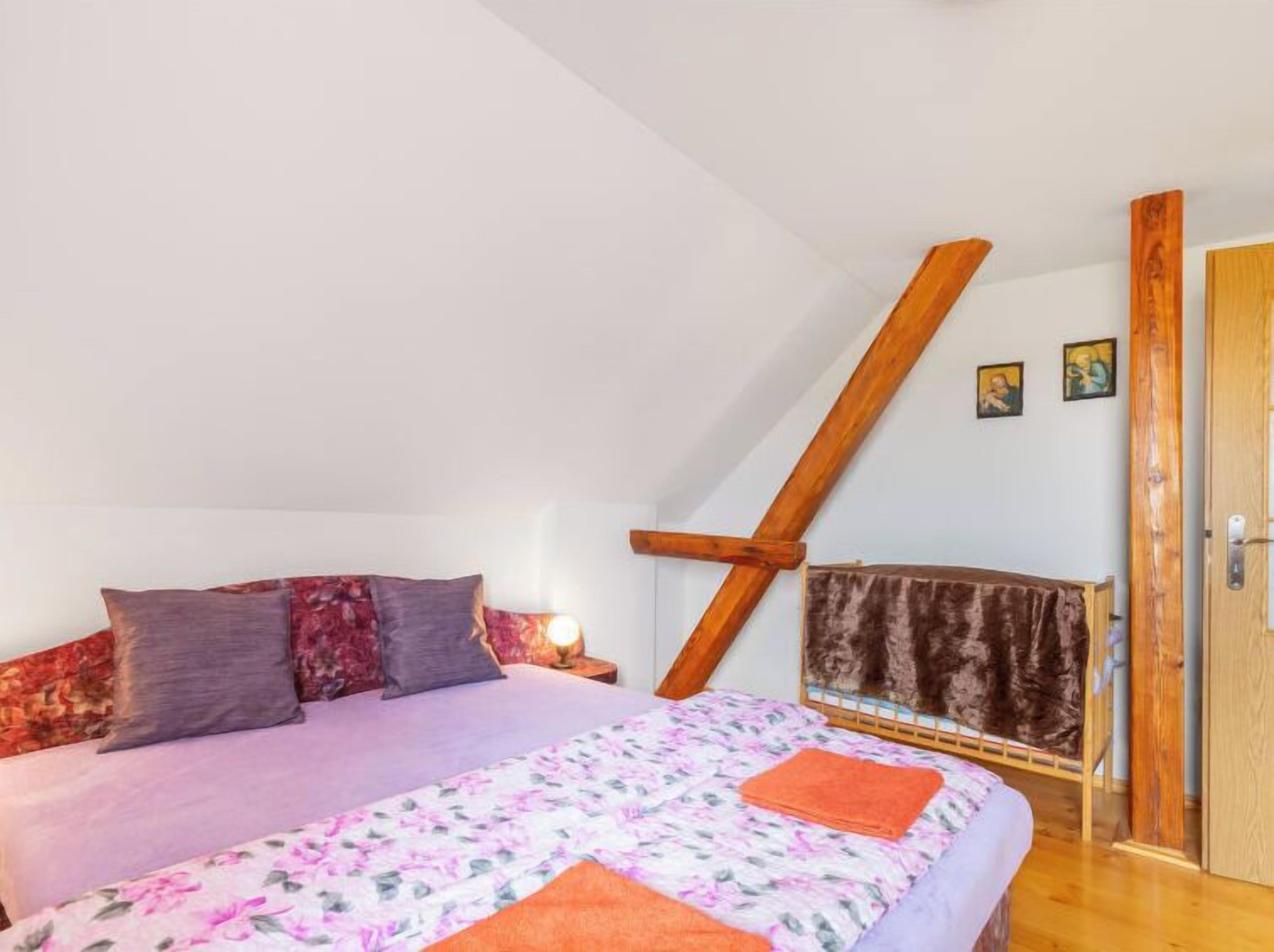 Une chambre avec un plafond en pente, un lit recouvert d’une literie à motifs floraux, une tête de lit en bois et une porte sur laquelle est accrochée une serviette.