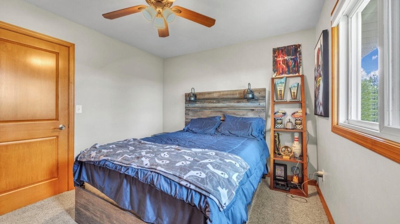 Une chambre à coucher avec un lit, un ventilateur de plafond, une fenêtre et une bibliothèque.