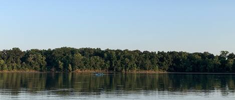 A calm lake with a forested shoreline and a small boat in the distance.
