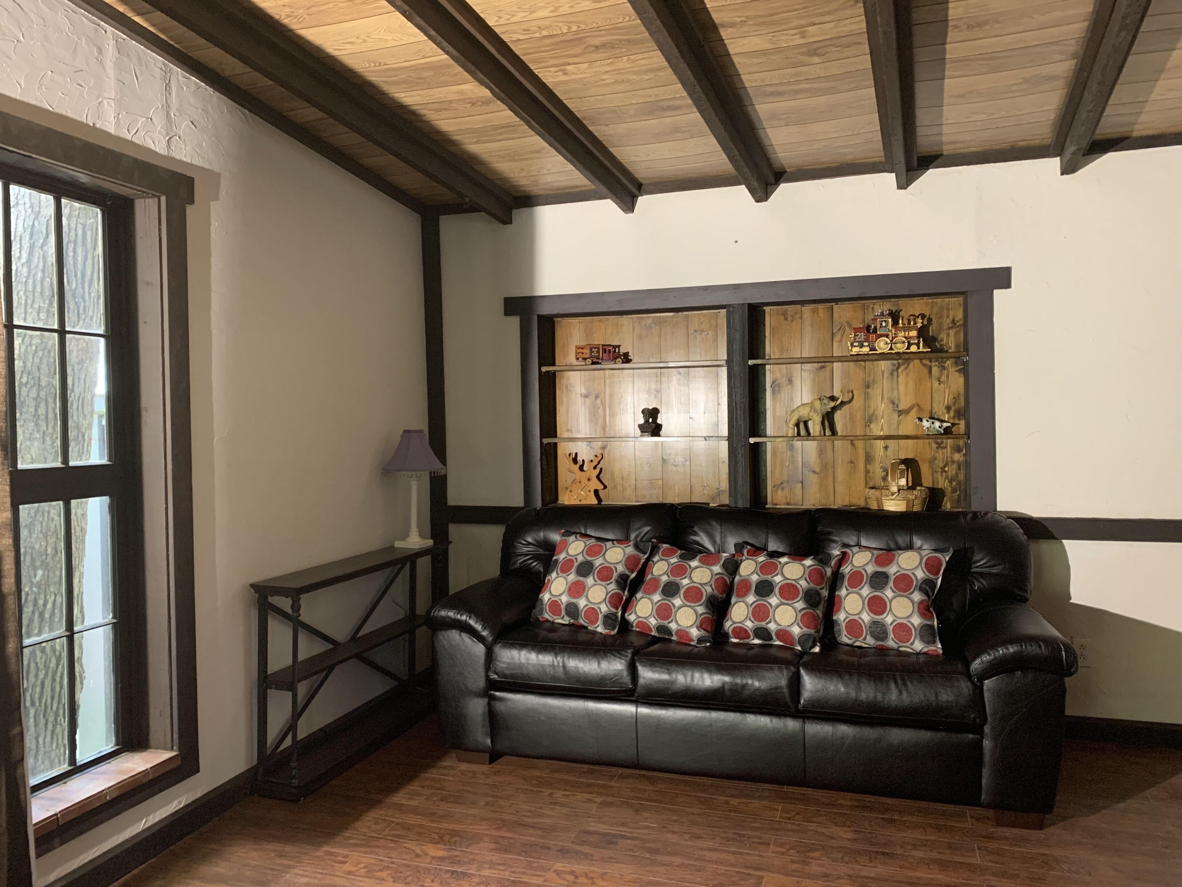 Une pièce avec un canapé en cuir noir, des étagères en bois ornées d’objets décoratifs et une fenêtre offrant une belle vue.
