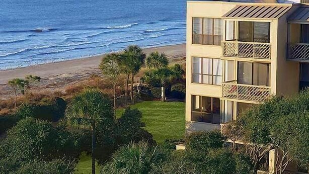 A coastal building with a view of the ocean, a balcony, and a well-maintained lawn. - Hilton Head | Family Island Stay | Pool + Beach | 2BR Condo (Hilton Head Island)