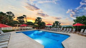 A swimming pool with lounge chairs and umbrellas, surrounded by trees and a sunset view. - Hilton Head | Family Island Stay | Pool + Beach | 2BR Condo (Hilton Head Island)