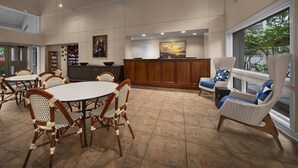A spacious dining area with round tables and wicker chairs, a reception desk, and a large window offering a view. - Hilton Head | Family Island Stay | Pool + Beach | 2BR Condo (Hilton Head Island)