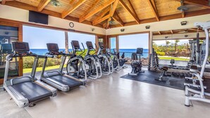 Une salle de sport équipée de tapis de course, de vélos d’exercice et de poids, offrant une vue panoramique sur l’océan.
