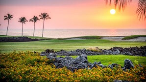 Un parcours de golf offrant une vue sur le coucher de soleil, bordé de palmiers et donnant sur un plan d’eau.