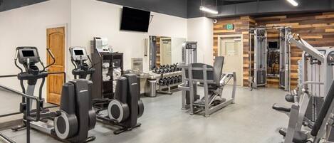 A gym with cardio machines, weightlifting equipment, and dumbbells.