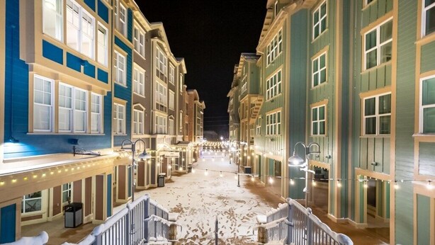 A snow-covered street with buildings on either side, illuminated by string lights.
