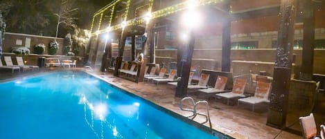 Una piscina con sillones de descanso y un área techada con guirnaldas de luces.