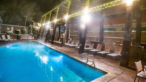 A swimming pool with lounge chairs and a covered area with string lights.