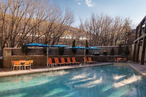 A swimming pool with lounge chairs and umbrellas, surrounded by a stone wall and trees.
