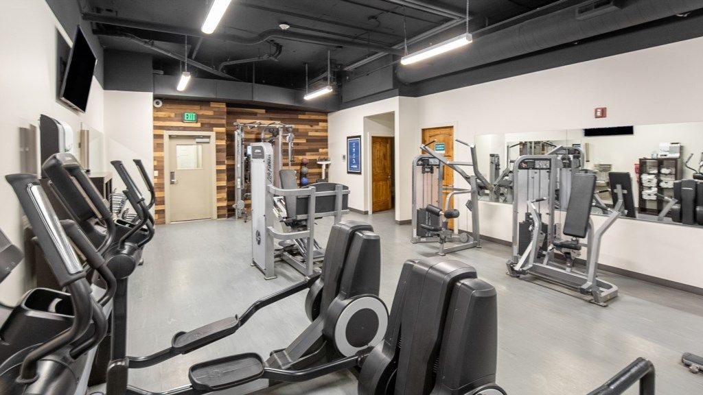 Une salle de sport moderne dotée de divers appareils d’exercice, d’un mur d’accent en bois et d’un intérieur propre et bien éclairé.