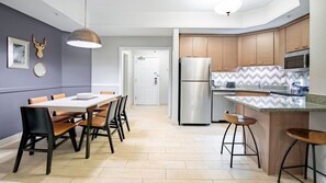 Cocina moderna con una isla central, electrodomésticos de acero inoxidable y un comedor con mesa y sillas.