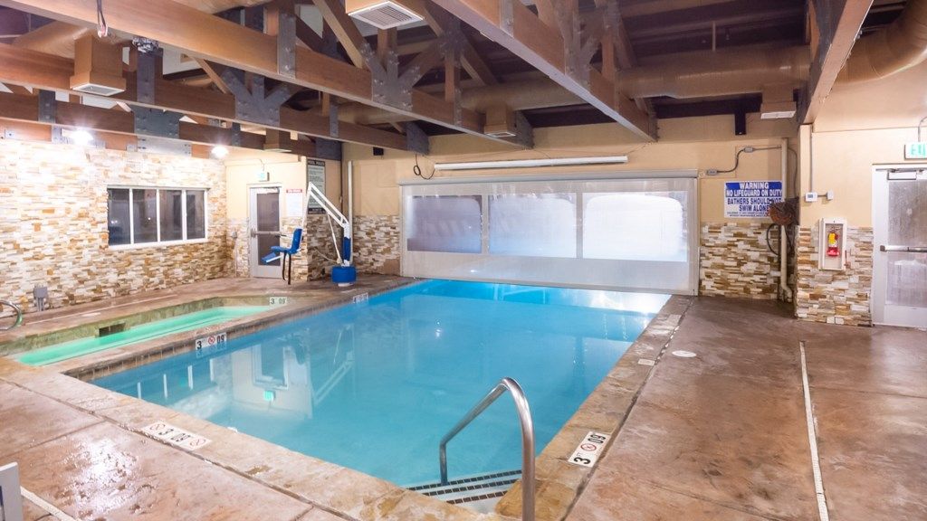 An indoor swimming pool with stone walls, a blue pool, and a wooden ceiling structure.