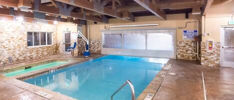 An indoor swimming pool with stone walls, a blue pool, and a wooden ceiling structure.