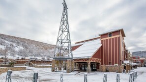 Um edifício coberto de neve com uma torre imponente, uma entrada protegida e montanhas ao fundo.