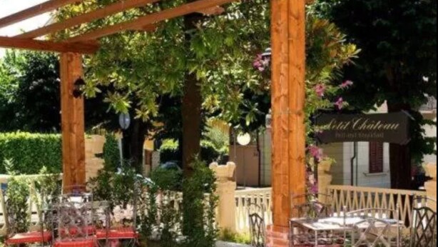 Une terrasse extérieure avec des tables et des chaises en métal, entourée de verdure et agrémentée d’une pergola en bois.
