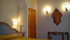 Une chambre d’hôtel avec un lit, une porte en bois, un miroir et des lampes fixées au mur.