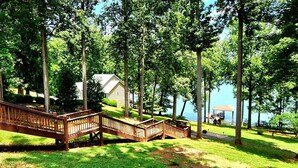 A wooden deck leading to a gazebo by a lake, surrounded by tall trees and a small building. - Almost There- Fire pit, dog friendly sleeps 6 (Moneta)