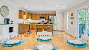A modern kitchen with wooden cabinets, stainless steel appliances, and a dining area with a table set for four. - Almost There- Fire pit, dog friendly sleeps 6 (Moneta)