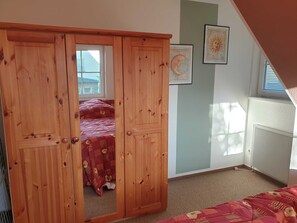 Un dormitorio con un armario de madera, una cama con colcha floral, una ventana con persianas y un radiador.
