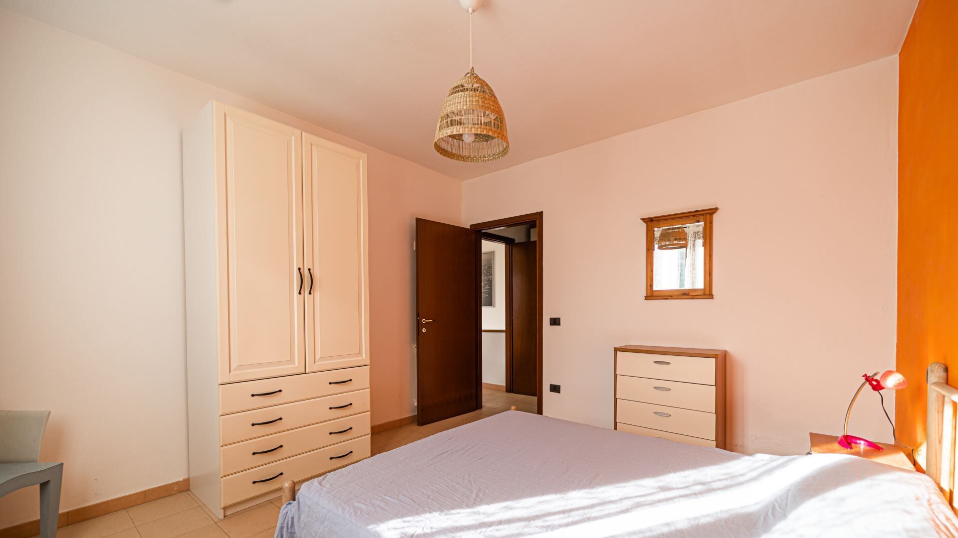 Une chambre à coucher comprenant un lit, une armoire, une table de chevet, un miroir et un luminaire suspendu.