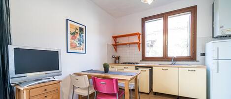 A compact kitchen with a dining area, a TV, and a window providing natural light.