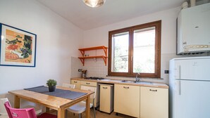 A compact kitchen with a wooden table, chairs, a sink, and a white refrigerator. - APP.TI LA BAIA BAGNAIA - BILOCALE ROSMARINO (Portoferraio)