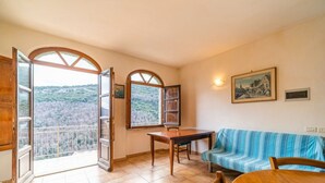 Una habitación con una mesa de madera, un sofá azul a rayas y dos ventanas con vistas a un paisaje boscoso.