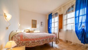 Un dormitorio con cama, escritorio, silla, espejo y ventana con cortinas azules.