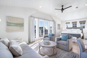 A spacious bedroom with a large bed, a ceiling fan, and a view of the outdoors through the windows.