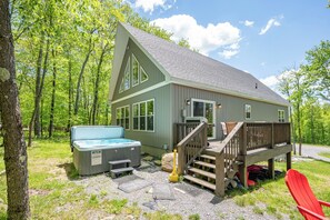 A cabin with a hot tub, deck, and outdoor seating area surrounded by trees.