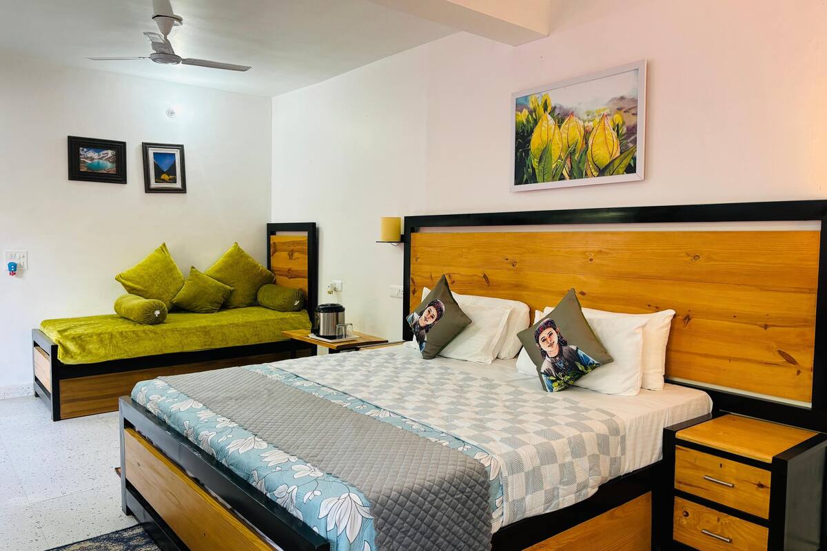 A bedroom with a large bed, a smaller sofa, a nightstand, and a ceiling fan.