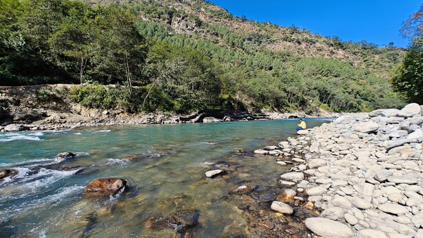 Un río serpentea por un paisaje rocoso, con una persona sentada sobre una roca a la orilla.