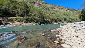 A river flowing through a rocky landscape with a person sitting on a rock by the water. - Vedant by the River - Chopta Gateway - By Himalayan Eco Lodges (Ukhimath)