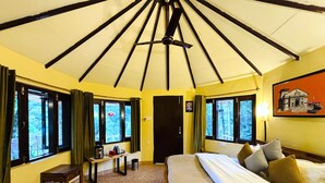 Una habitación con cama, una mesa con hervidor, un banco y una ventana con cortinas.