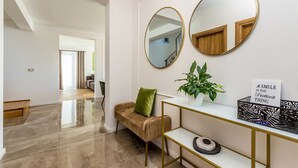 A modern interior with a hallway leading to a living area, featuring a sofa, a console table with a plant, and two wall-mounted mirrors.
