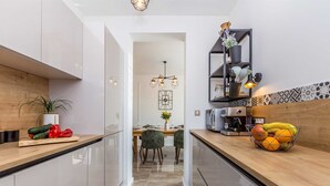 A modern kitchen with white cabinets, a wooden countertop, and a dining area with a chandelier.