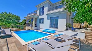 A two-story house with a swimming pool, outdoor seating, and a stone wall.