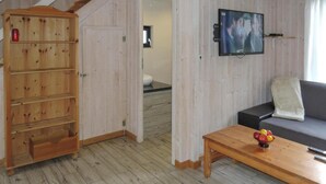 Un meuble en bois avec plusieurs tiroirs, un téléviseur fixé au mur, un canapé avec un coussin et une table basse avec des fruits.