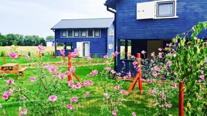 Une maison bleue avec un porche et un jardin où poussent des fleurs roses.