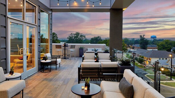 A modern outdoor patio with seating, a view of the city, and string lights. - AC Hotel by Marriott Tuscaloosa Downtown (Tuscaloosa)