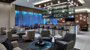 A modern hotel lobby with a bar area, seating arrangements, and a large window offering a view. - AC Hotel by Marriott Tuscaloosa Downtown (Tuscaloosa)