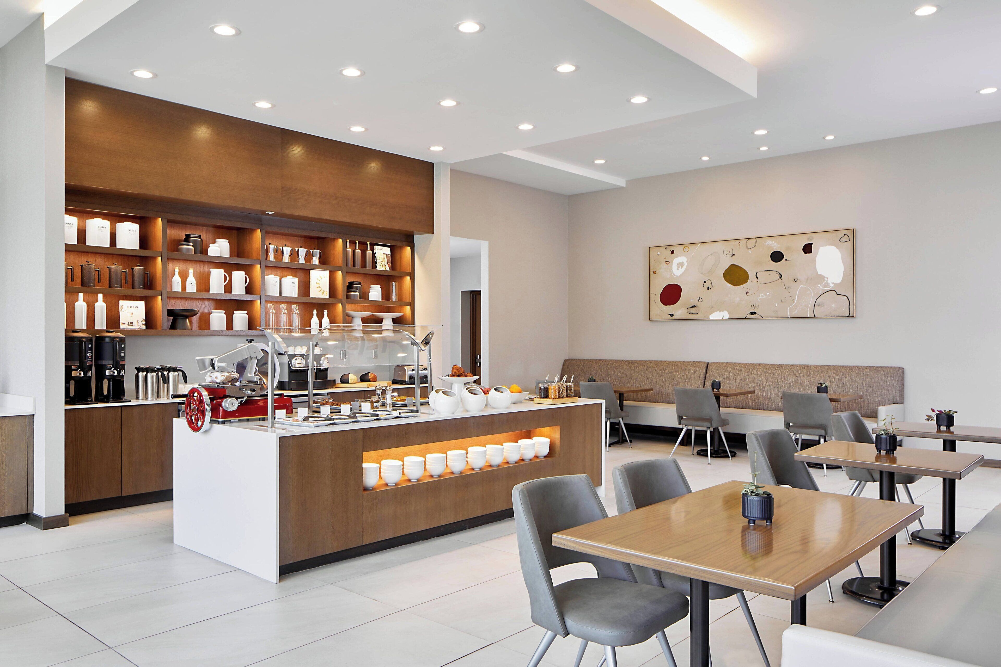 A modern cafe with a central counter, seating area, and a wall-mounted abstract art piece.