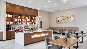 A modern cafe with a central counter, seating area, and a wall-mounted abstract art piece.