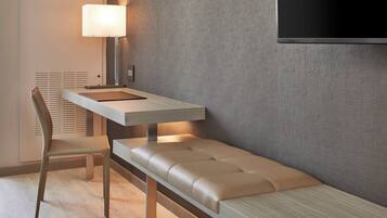 Una habitación moderna con una banca, un escritorio, una silla, una lámpara y un televisor instalado en la pared.