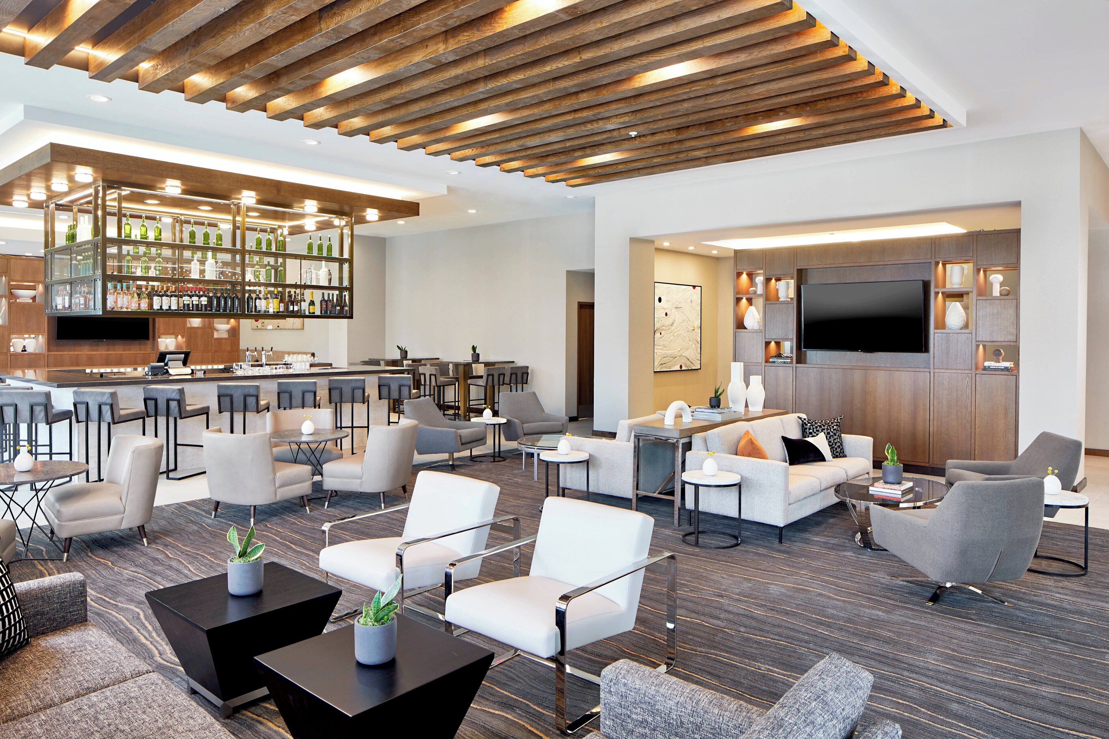 Um saguão de hotel moderno com área de bar, assentos e uma TV de tela plana.