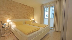 Ein Hotelzimmer mit zwei Betten, einer Ziegelwand, einem Fenster mit Vorhängen und einem Nachttisch mit Lampe.