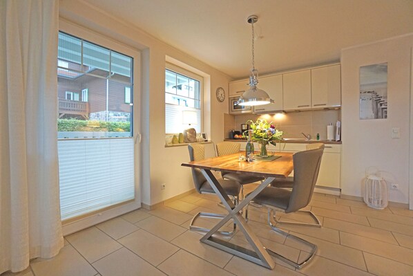 A modern kitchen with white cabinets, a wooden dining table, and a hanging light fixture.